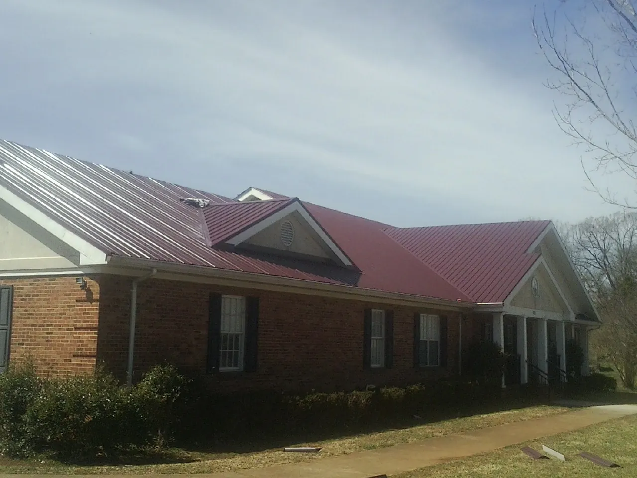 Red metal roof with gabled entries on a long brick building, from a Hail Damage Roof Repair job in Barre