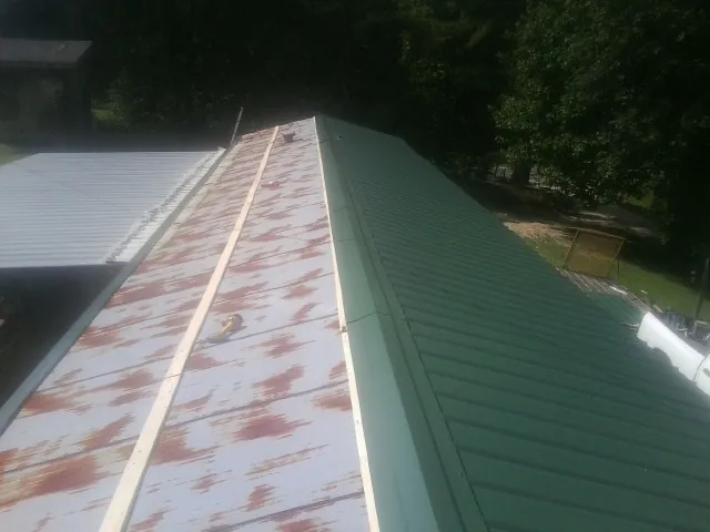 Old rusted panels beside newly installed green metal roofing — Wind Damage Roof Repair by Roofing Brothers in Barre