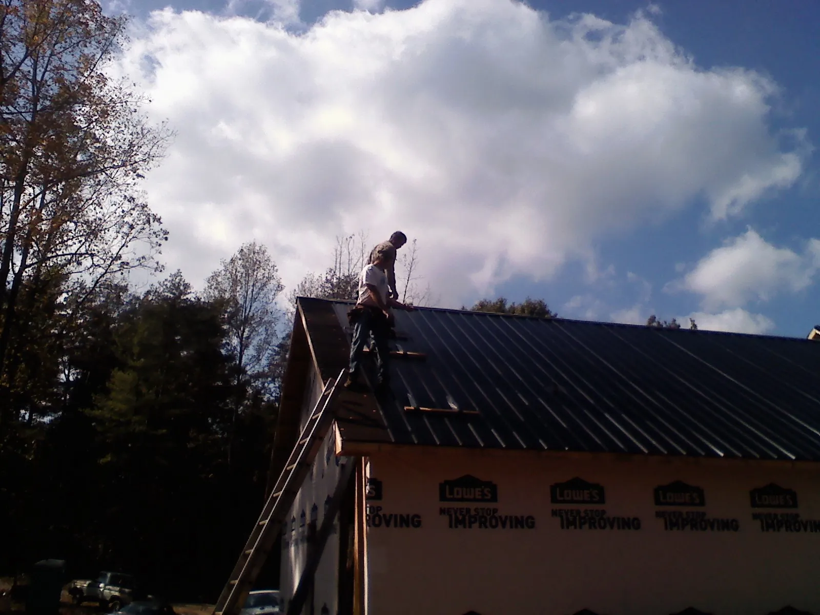Roofer fastening dark metal panels high against a cloudy sky, from a Roof Inspection job in Barre