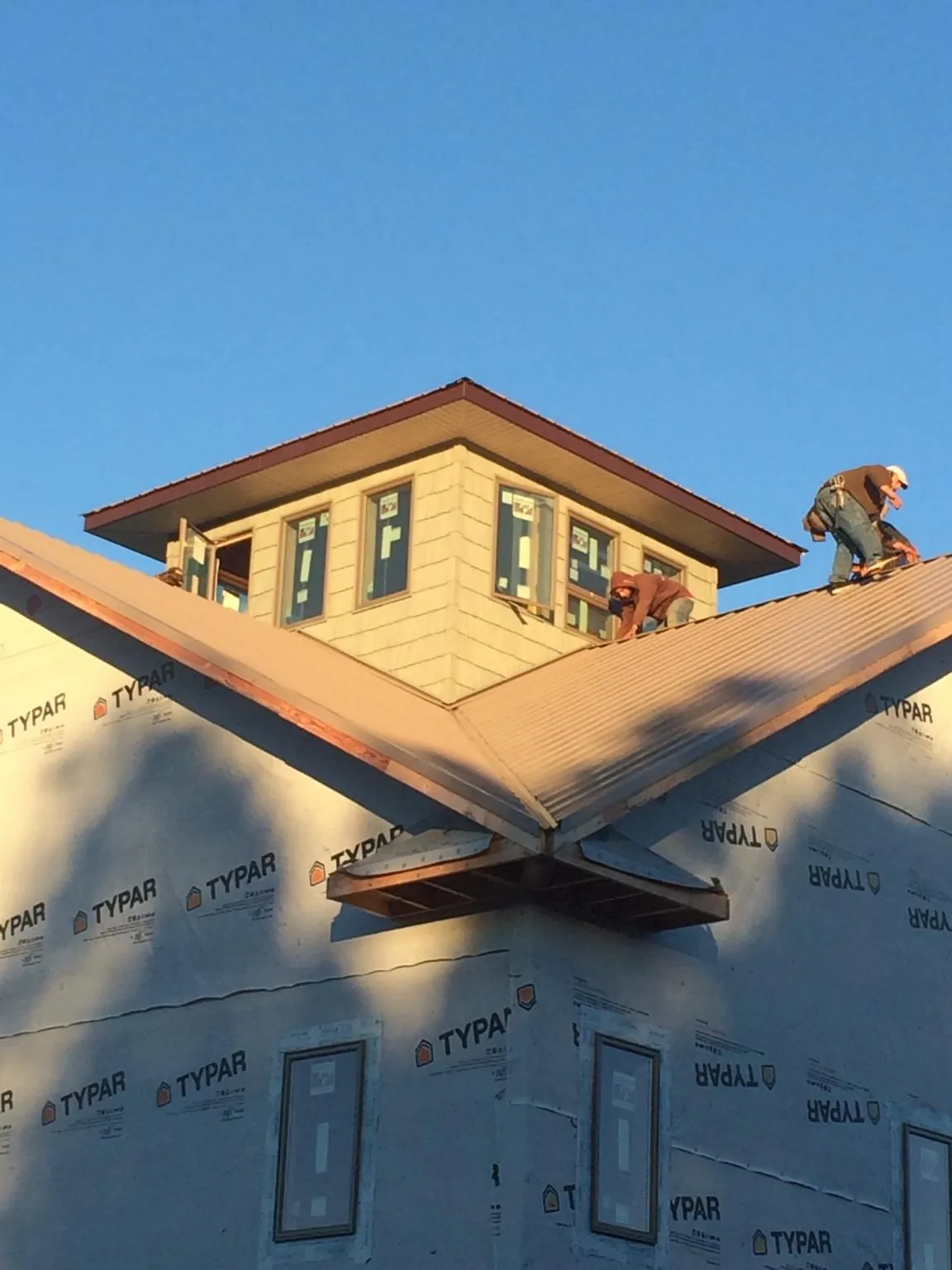 Roofers working around a rooftop cupola on a new metal roof at sunset — Roof Waterproofing in Barre by Roofing Brothers